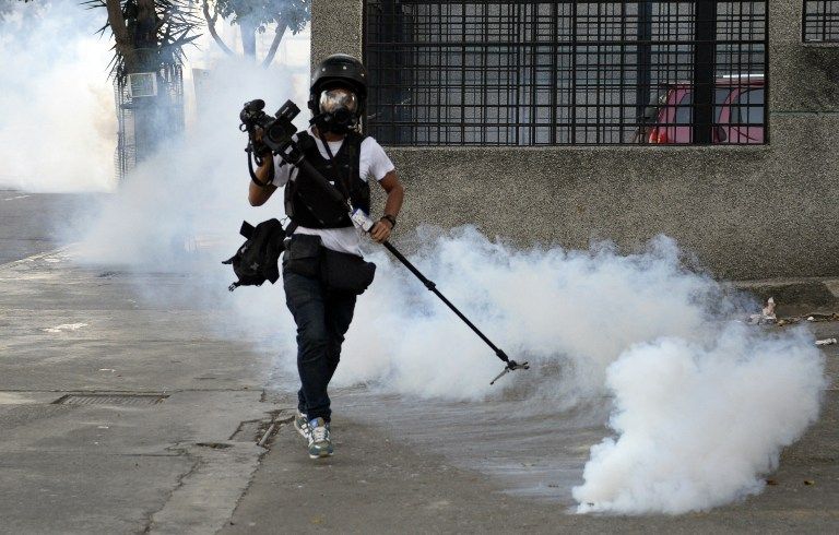Cameraman runs away from tear gas during an anti-government protest in Caracas on February 22, 2014. Hundreds of thousands of Venezuelans took to the streets of Caracas in marches for and against President Nicolas Maduros government Saturday, as the nati